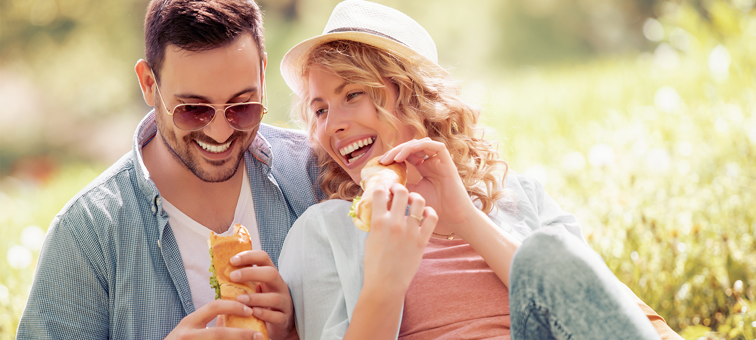 Hämorrhoiden vorbeugen durch Präventivmaßnahmen, Verhaltens- und Ernährungsempfehlungen. Paar sitzt in einer Wiese und macht ein Picknick.